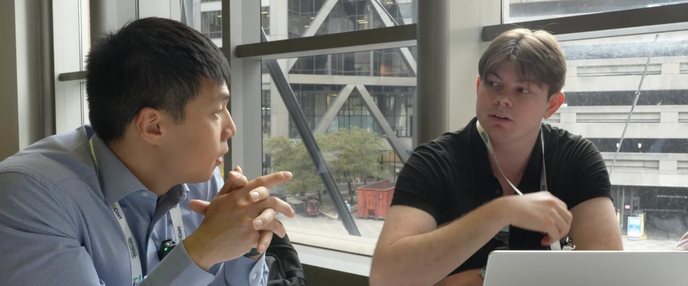 Jonathan Oh in conversation with Hadley Nelson at a table by a window, laptop open